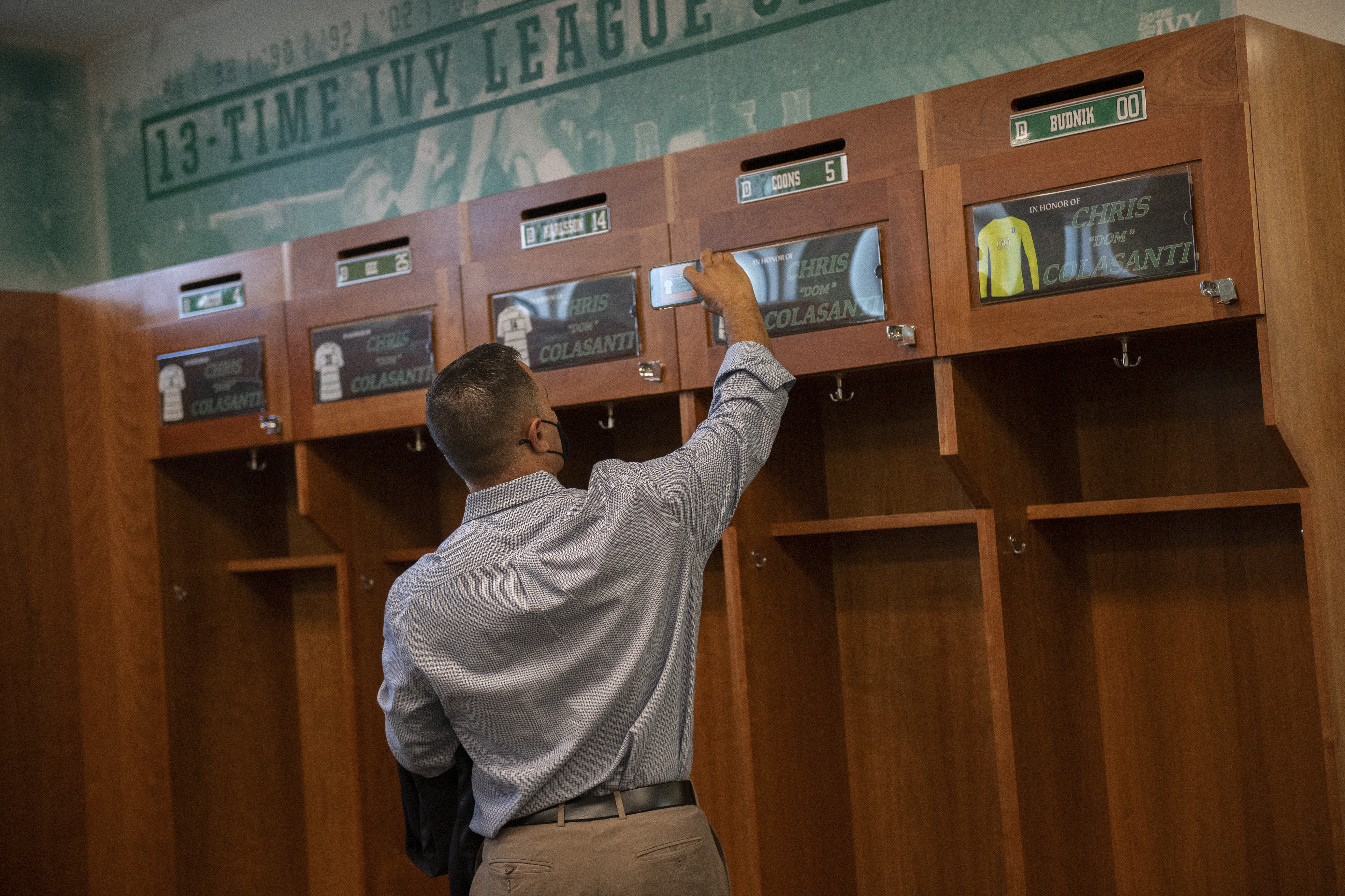 A man takes a picture of the men's soccer locker room with name plates honoring Chris "Dom" Colasanti