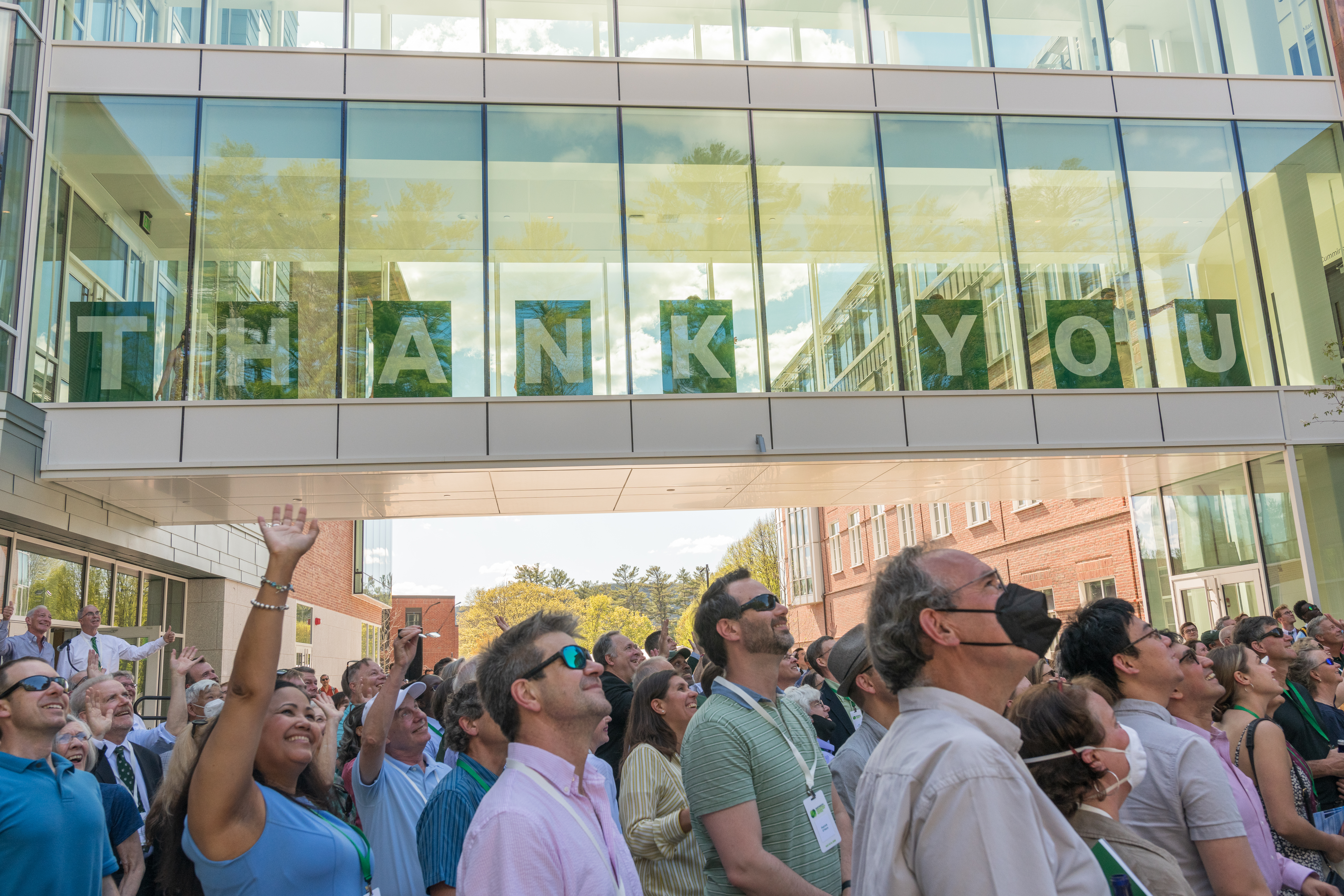 ECSC dedication guests wave to a drone shot above. The letters Thank You are spelled out in the building's glass bridge