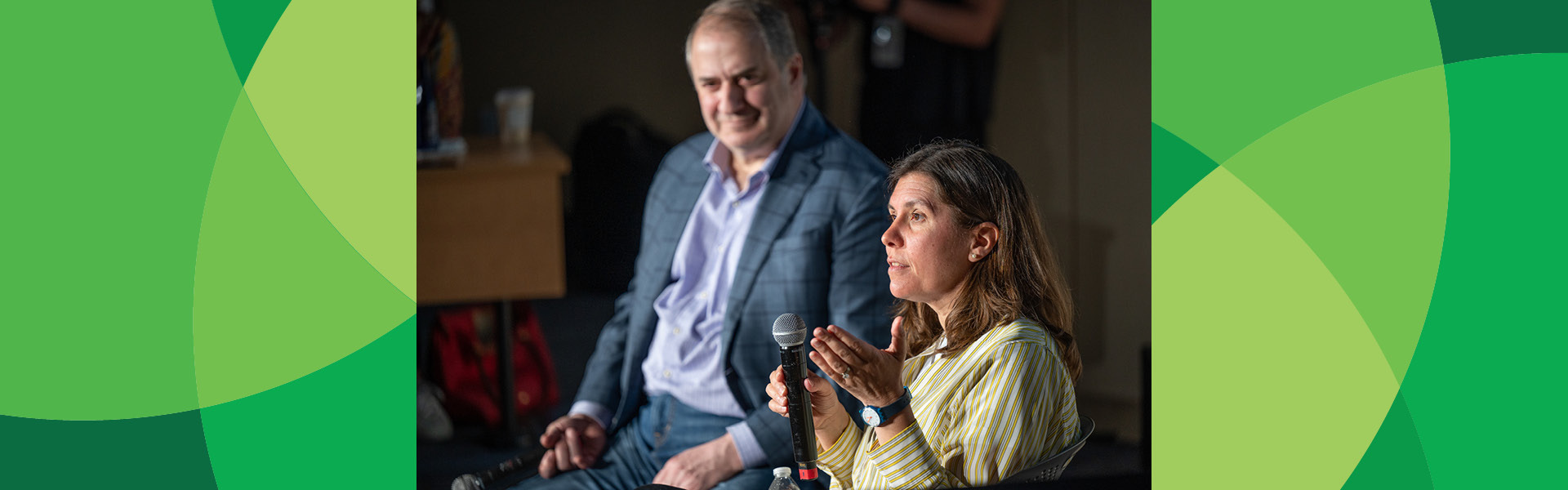 Kristen Morrow Johnson holding a microphone and speaking, seated next to Bill Helman