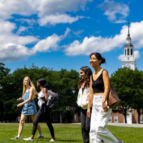 A group of four students walking across the Green on a sunny day.