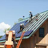 Workers install solar panels on a roof