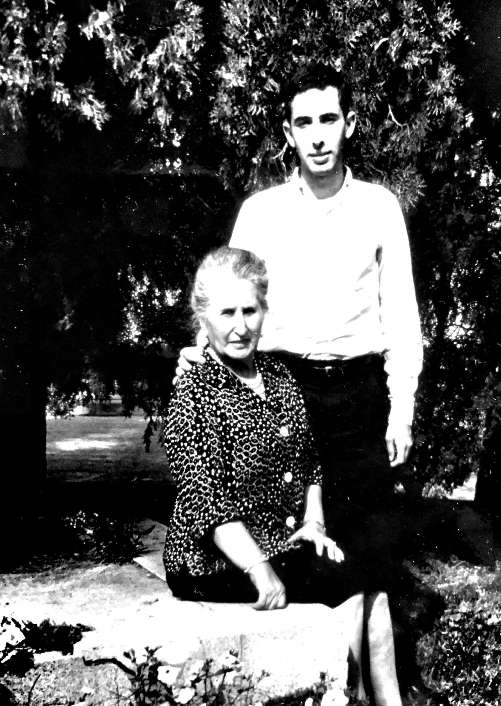 A young man stands next to an older woman, who is seated.