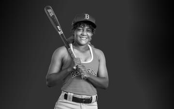 Bianca Smith ’12 black and white photo holding a baseball bat wearing red sox gear
