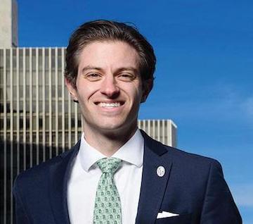 A smiling man wearing a suit in front of an urban skyline