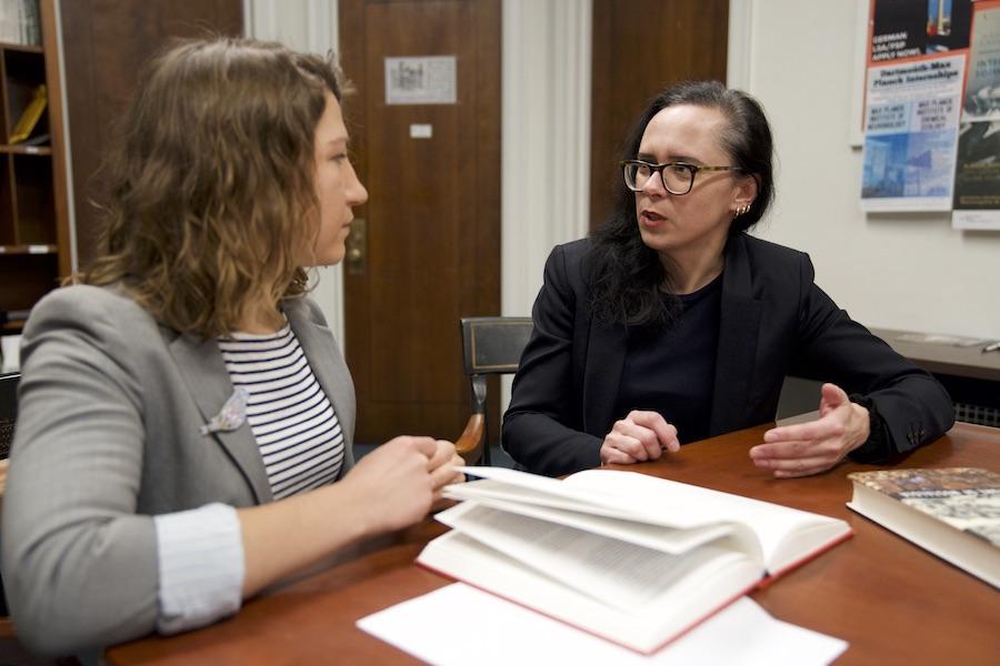 Two women speak while looking at academic texts.